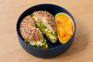 Mini-bagel met ei, maïs en sla, met sinaasappelpartjes.