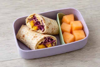 Platbroodrolletjes met hummus, geroosterde paprika en rode kool, met meloen.